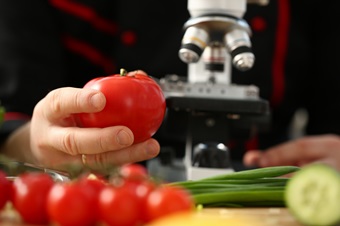Researcher holding tomato in front of microscope
