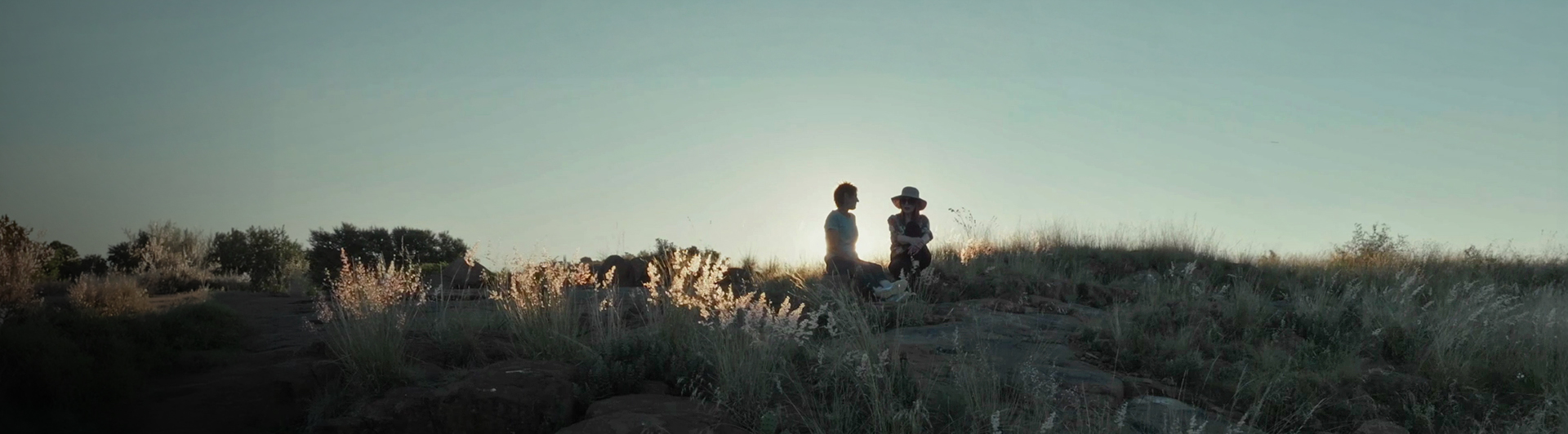Two people sitting on a hill side.