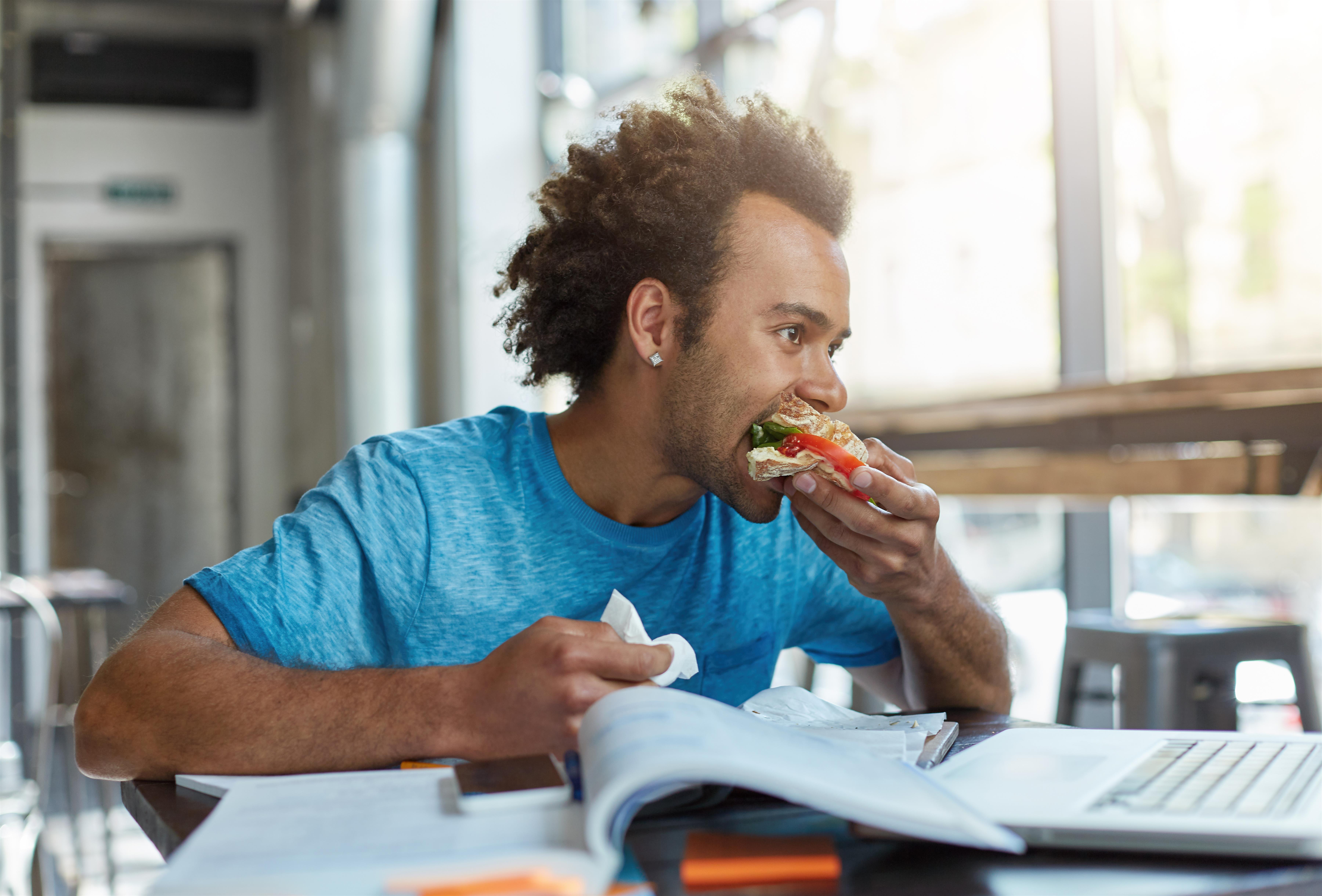 black-mixed-race-male-student-being-busy-with-studying-resting-minute-eating-sandwich